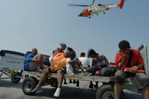 Airport luggage carriers are employed as a means to transport evacuees to the main passenger terminal at the Louis Armstrong International Airport, in New Orleans, Louisiana (LA), as rescue efforts are underway in the aftermath of Hurricane Katrina. A US Coast Guard (USCG), HH-65A Dolphin helicopter is visible in the background. Department of Defense (DOD) units are mobilizing as part of Joint Task Force (JTF) Katrina to support the Federal Emergency Management Agency's (FEMA) disaster-relief efforts in the Gulf Coast areas devastated by Hurricane Katrina