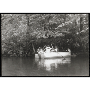 Five youth and a supervisor raise their hands in the air while sitting in a rowboat