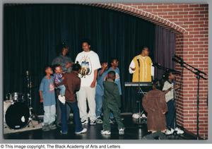 Photograph of two men, a woman, and a group of children on a stage