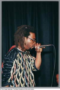 Photograph of the right side of man, holding a microphone close to his face