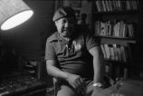 Gaines seated talking in front of bookshelves (EGP-9 #292)