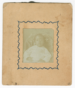 Photograph of a baby dressed in white and sitting in a chair