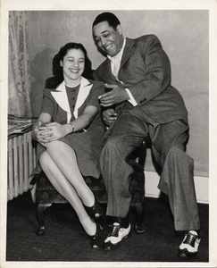 Beatrice Ellis; AKA Evie Ellington sitting in a chair with Duke Ellington sitting on the arm of the chair : black-and-white photoprint.