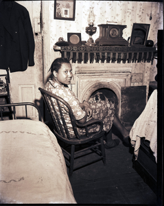 Woman seated before fireplace: black-and-white photonegative.