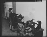 Manning Office of War Information's "nerve center." A new field of employment was opened to Negroes recently when six colored girls were given skilled jobs in the teletype room of the OWI. The young women, trained by OWI at the American Telephone and Telegraph School in Washington, D.C., operate machines which receive and send official war information to all parts of the country. Miss Esther V. Myers is shown at a receiving machine in the teletype room of the Bureau of Publications and Graphics while Miss Shirley K. Conway dispatches news on an ASR machine