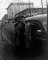 African-American couple standing next to a car near the Bush Hotel on Jackson St. and 6th Ave., Seattle, ca. 1950's