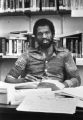 Howard Fuller sits at a desk in his office, in front of shelves covered with books, circa 1980