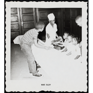 Two boys serve food and drinks to three girls sitting at a table during a Boys' Club Little Sister Contest