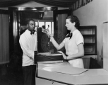 Woman working on a cash register while a waiter looks on.