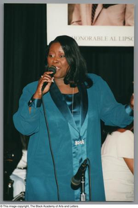 Photograph of a woman in a velvet suit, singing into a microphone