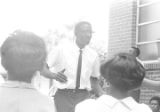 Dan Houser speaking to a group of people standing outside a brick church building in Prattville, Alabama, during a meeting of the Autauga County Improvement Association.